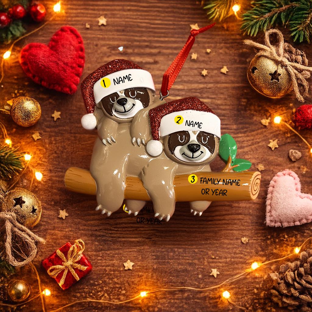 Two sloth ornaments on a branch with Christmas decorations on a wooden surface.