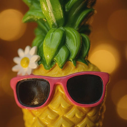 Pineapple with pink sunglasses and a flower on a blurred background
