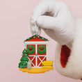Load image into Gallery viewer, Hand wearing a white glove holding a Christmas-themed ornament on a pink background
