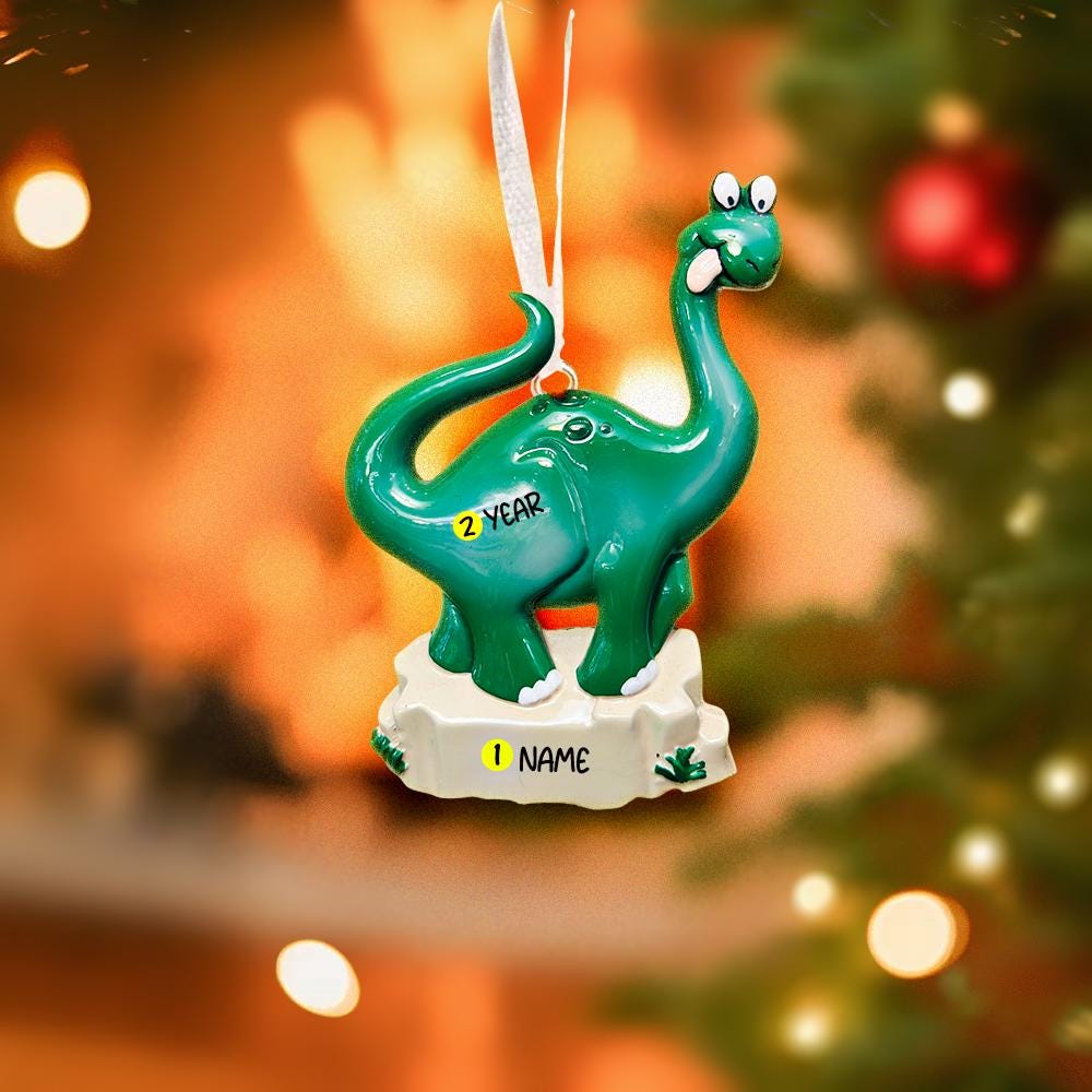 Green dinosaur ornament with customizable text on a blurred Christmas tree background