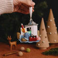 Load image into Gallery viewer, Hand holding a Christmas ornament with a person on a ski lift against a festive background.
