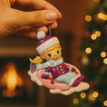 Load image into Gallery viewer, Christmas ornament of a girl on a sled held by a hand with a blurred festive background.
