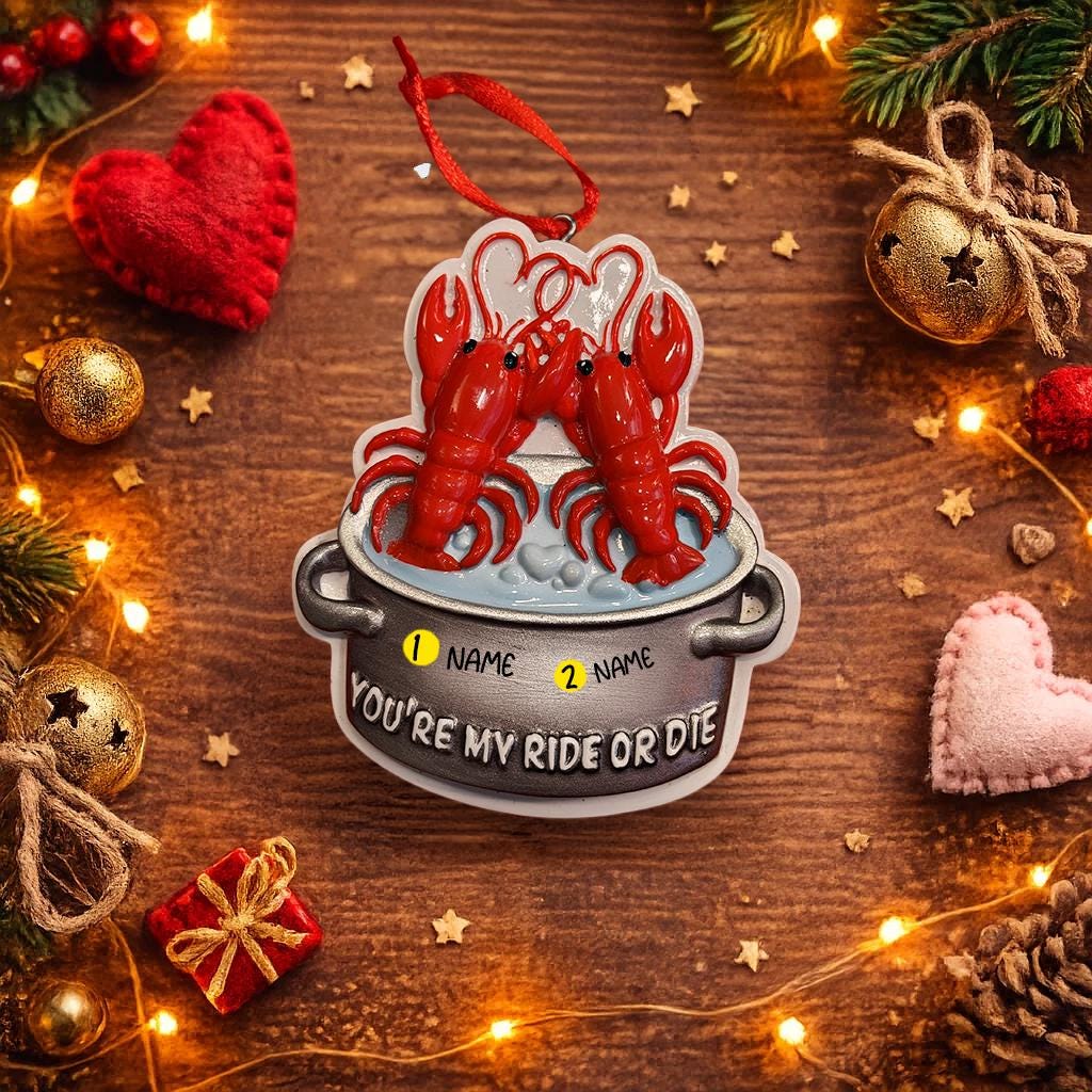 Decorative ornament with two lobsters in a pot on a wooden surface with Christmas decorations.