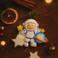 Load image into Gallery viewer, Personalized astronaut Christmas ornament featuring a detailed 3D front design with a smiling space explorer holding a colorful planet and bright yellow stars. The child’s name is added on the suit and the year is written on the star for a custom touch. This space themed ornament is perfect for kids who love rockets, planets, and outer space dreams. A fun and meaningful holiday keepsake for future astronauts and little space lovers.
