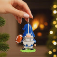 Load image into Gallery viewer, Personalized football gnome Christmas ornament featuring a blue and white gnome character wearing a football helmet and holding a football, customizable name area on the front body and customizable year area on the football, glossy finish with raised 3D front details and flat 2D back, white hanging ribbon, displayed on a snowy football field themed holiday background with pine branches and festive decorations.
