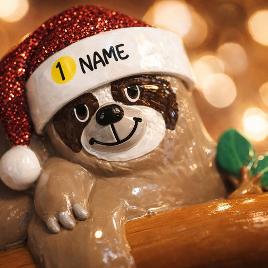 Decorative sloth figurine wearing a Santa hat with 'NAME' label against a blurred light background