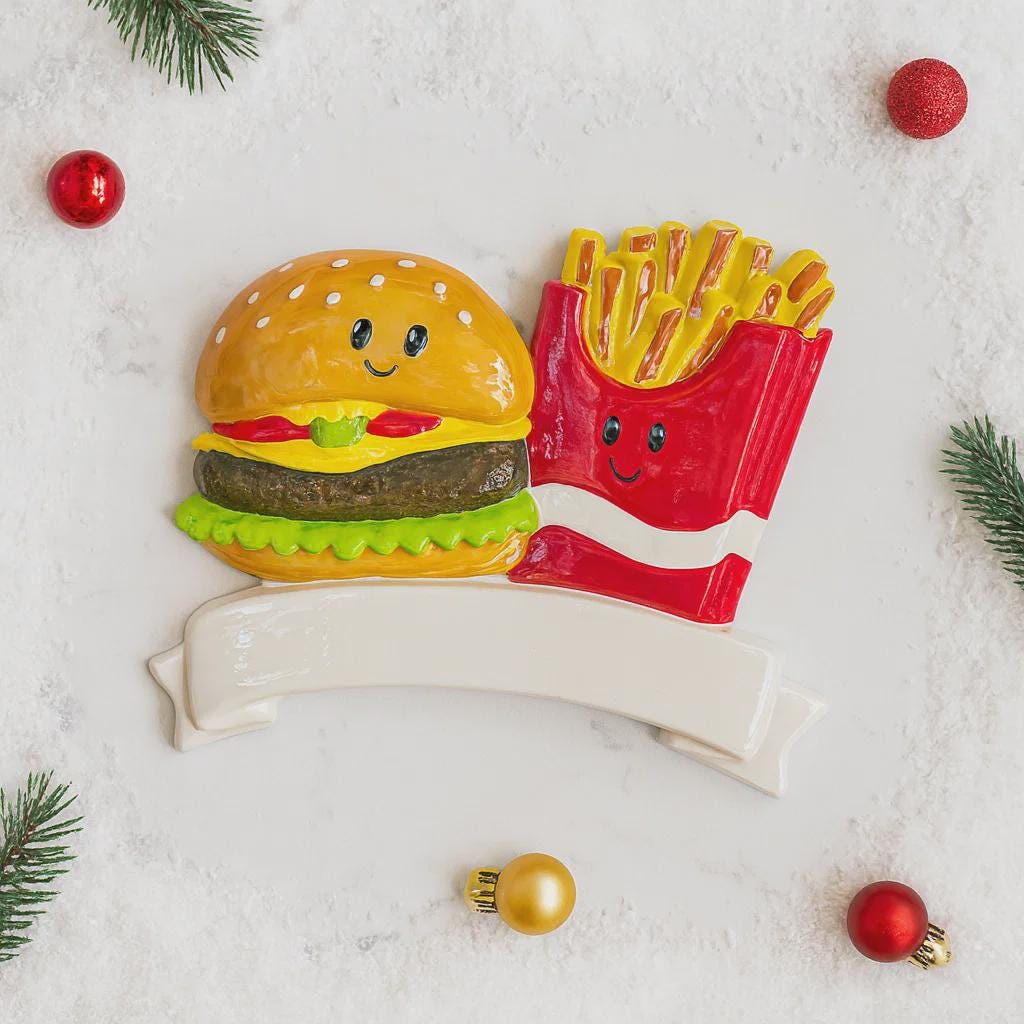 Decorative Christmas ornament shaped like a burger and fries on a snowy background with ornaments.