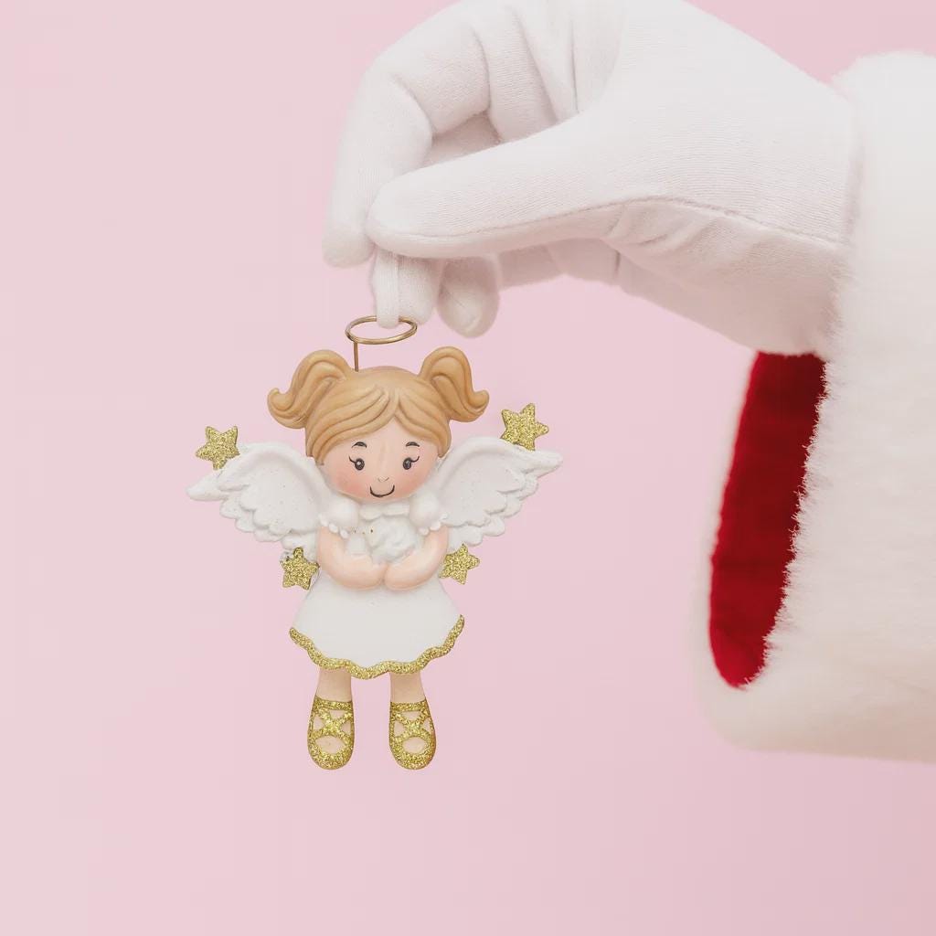 Decorative angel ornament held by a gloved hand on a pink background