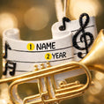 Load image into Gallery viewer, Personalized music ornament featuring a white musical staff design with black notes and a gold trumpet detail. Includes free handwritten personalization with one name and year written on the sheet music. Shown hanging with a ribbon in a warm festive holiday setting with soft lights instruments and seasonal decor. Designed with a 3D raised front and flat back perfect for Christmas tree display and gifts for musicians music lovers and band members.
