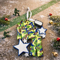 Load image into Gallery viewer, A glossy resin Army soldier uniform ornament in green brown and blue camouflage colors features a military jacket and pants shape with raised buttons and pockets, white and blue star accents, light snow texture, a smooth painted cartoon style finish, and handwritten personalization showing a name and year on the attached tag, designed as a mostly 2D ornament with raised 3D details on the front only for Christmas tree decor.
