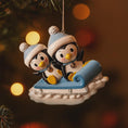 Load image into Gallery viewer, Decorative ornament of two penguins on a sled with festive lights in the background
