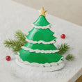 Load image into Gallery viewer, Green Christmas tree-shaped cookie with a gold star on a white surface with pine branches and red berries.
