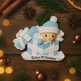 Load image into Gallery viewer, Personalized Baby Boy First Christmas Ornament featuring an adorable baby popping out of a blue gift box with a matching hat and pacifier. The name is displayed on the hat while the year is placed on the ribbon detail, with Baby’s 1st Christmas written along the base. Soft blue and white tones, raised 3D elements, and sweet holiday details make this a charming keepsake. Perfect for newborn boys, baby showers, and celebrating a baby’s very first Christmas season.

