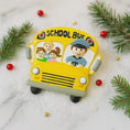 Load image into Gallery viewer, Yellow school bus-shaped toy with cartoon characters on a snowy background with Christmas decorations.
