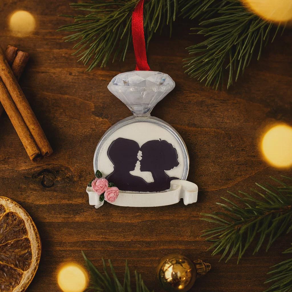 Decorative ornament with a diamond ring and silhouette of a couple on a wooden surface with Christmas decorations.