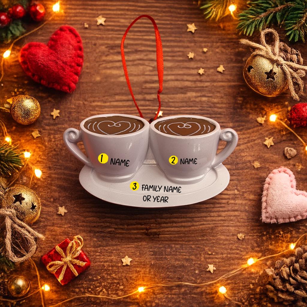 Two white mugs with personalized names on a wooden surface with Christmas decorations.