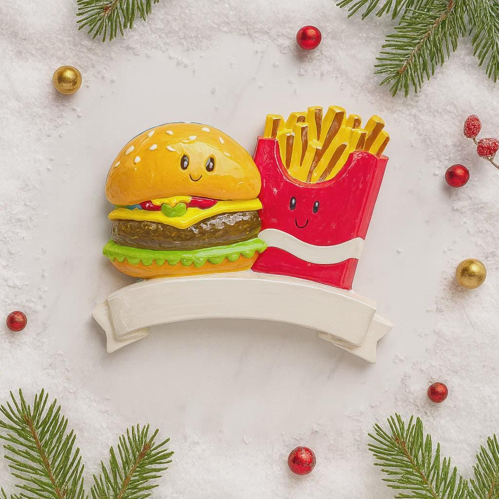 Decorative ornament shaped like a hamburger and fries with a banner on a snowy background.