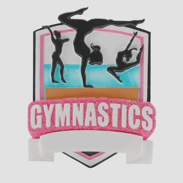 Personalized gymnastics Christmas ornament featuring elegant gymnast silhouette figures in motion, customizable name area on the front banner and customizable year area above the banner, glossy finish with raised 3D front details and flat 2D back, white hanging ribbon, displayed on a soft pink snowy holiday background with festive ornaments greenery and warm Christmas decor.
