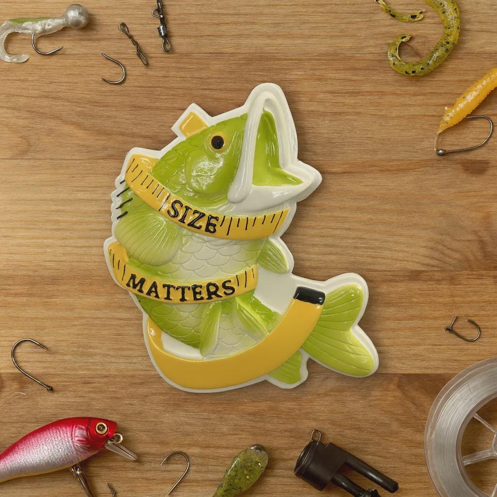 Decorative fish-shaped sign with 'Size Matters' on a wooden surface with fishing equipment.