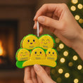 Load image into Gallery viewer, Hand holding a family-themed ornament with smiling faces in front of a warm, blurred background.
