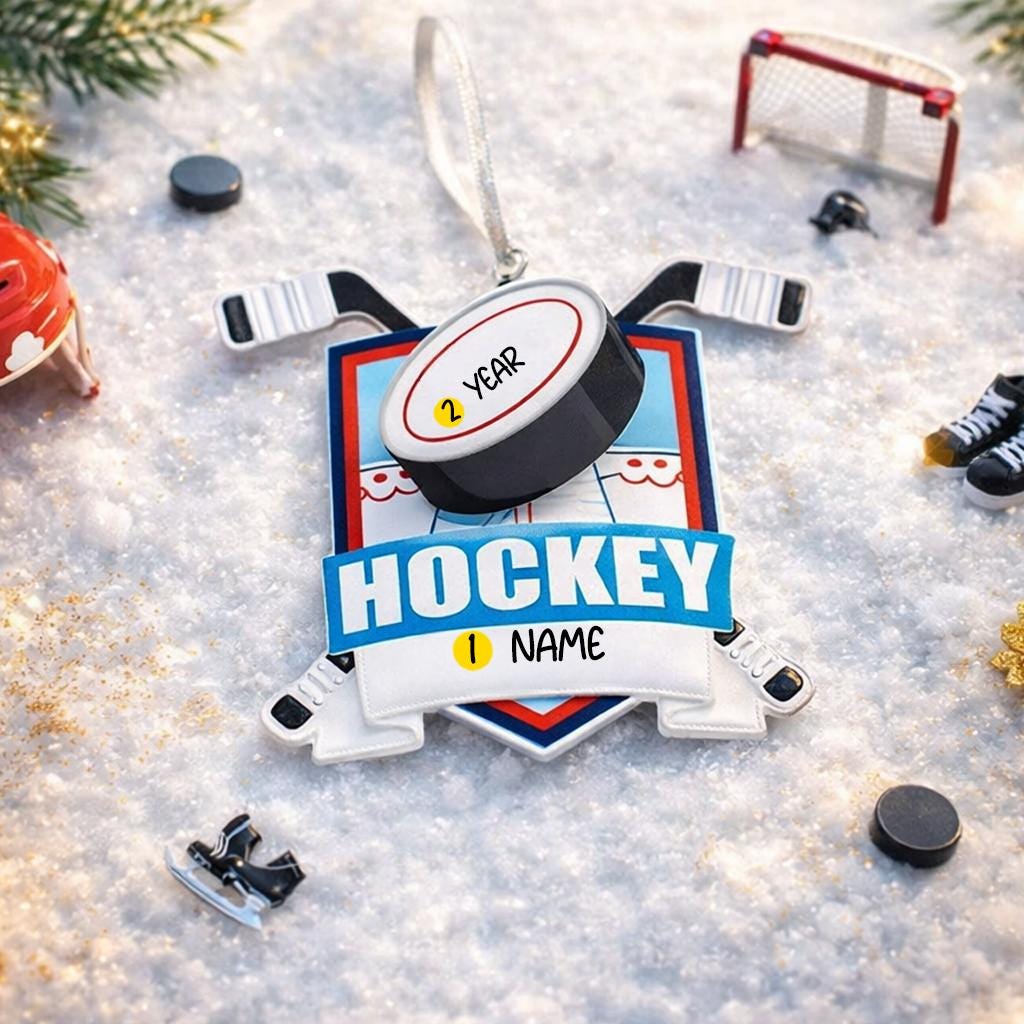 Personalized hockey Christmas ornament featuring a hockey puck and crossed hockey sticks design, customizable name area on the front banner and customizable year area on the puck, glossy finish with raised 3D front details and flat 2D back, white hanging ribbon, displayed on a snowy ice rink themed holiday background with hockey accessories and festive winter decorations.