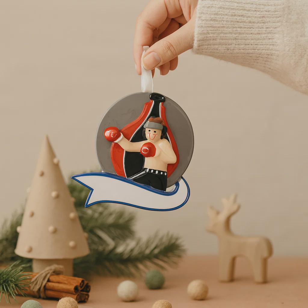Decorative Christmas ornament with a boxer design held by a hand, surrounded by festive items on a neutral background.