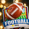 Load image into Gallery viewer, Personalized football Christmas ornament featuring a brown football with stitched details on a shield style background and goalpost design, customizable name area on the front banner and customizable year area on the football, glossy finish with raised 3D front details and flat 2D back, white hanging ribbon, displayed on a snowy football field themed holiday background with pine branches and festive decorations.
