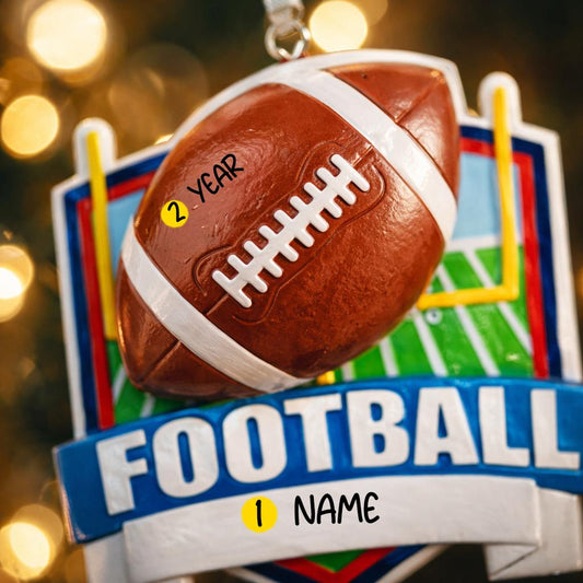 Personalized football Christmas ornament featuring a brown football with stitched details on a shield style background and goalpost design, customizable name area on the front banner and customizable year area on the football, glossy finish with raised 3D front details and flat 2D back, white hanging ribbon, displayed on a snowy football field themed holiday background with pine branches and festive decorations.