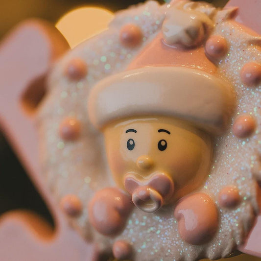 Decorative ornament item with a cartoonish face and pink hat on a glittery background