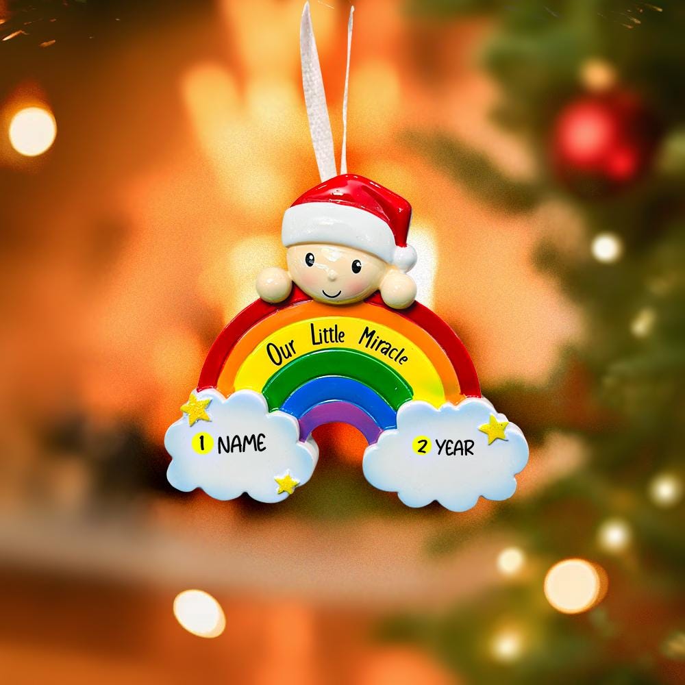 Decorative ornament with a baby figure and rainbow, placed on a Christmas tree.