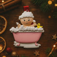 Load image into Gallery viewer, Decorative ornament of a baby in a bathtub with a duck, surrounded by Christmas decorations on a wooden surface.
