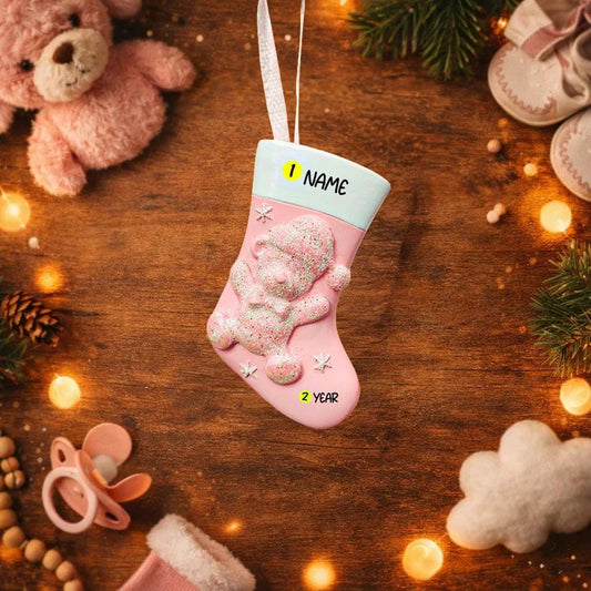 Pink Christmas stocking ornament with bear design on a wooden surface with festive decorations.