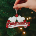 Load image into Gallery viewer, Personalized grandparents Christmas ornament featuring two white heart shapes with custom names, red rose details, glitter red grandchildren lettering and a heartfelt we love you message, designed as a sentimental holiday keepsake for grandparents, displayed on a warm rustic wooden background with cozy Christmas lights, ornaments and festive decor, perfect for celebrating family love and cherished memories during the holiday season
