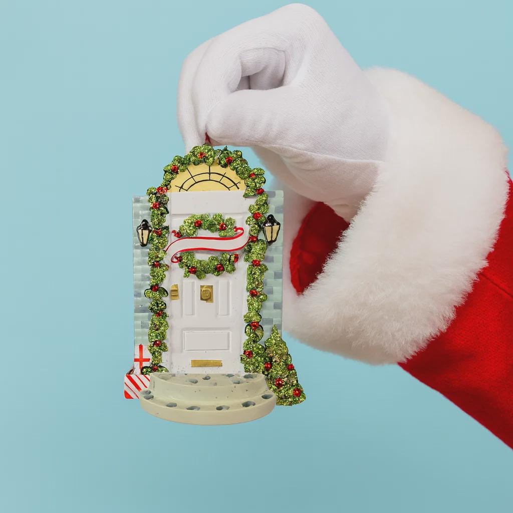 Hand wearing a Santa glove holding a Christmas door ornament against a light blue background