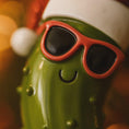 Load image into Gallery viewer, Green character with red sunglasses and a white hat on a blurred background
