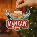 Load image into Gallery viewer, Man cave themed personalized ornament featuring a bold red Man Cave sign design with raised 3D details including beer mugs antlers sports icons and hobby elements. The ornament allows name personalization on the top area and year personalization at the bottom making it a fun and meaningful keepsake. Designed with a flat back for easy hanging this ornament is perfect for man cave decor Christmas trees or gift displays. Ideal for dads husbands boyfriends and anyone who loves their personal space traditions an
