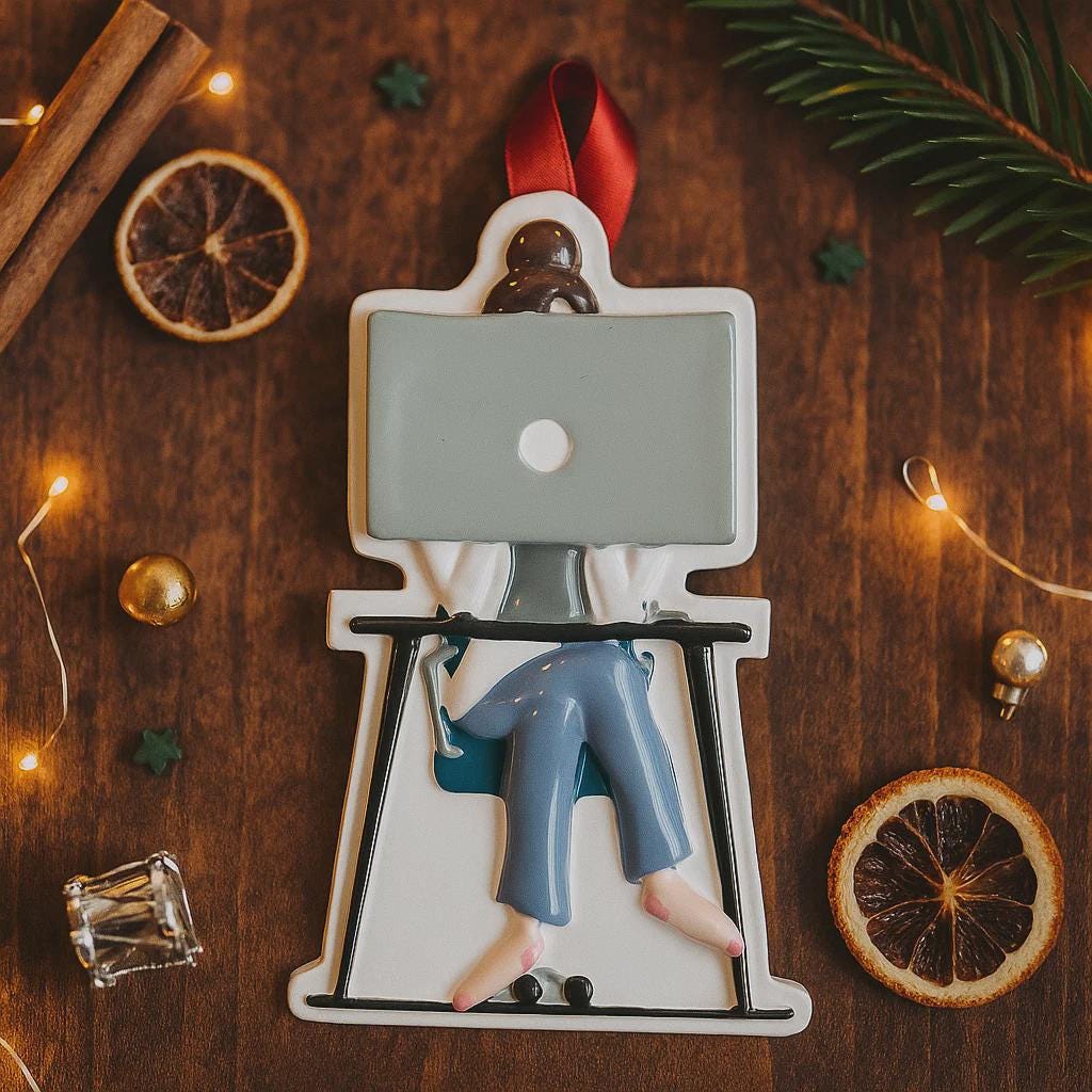 Decorative ornament of a person using a laptop on a wooden surface with Christmas decorations.