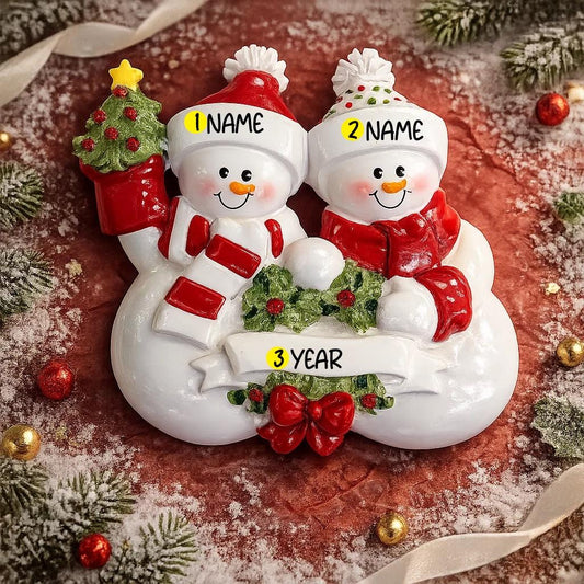 Personalized snowman couple ornament with customizable names and year, surrounded by Christmas decorations.