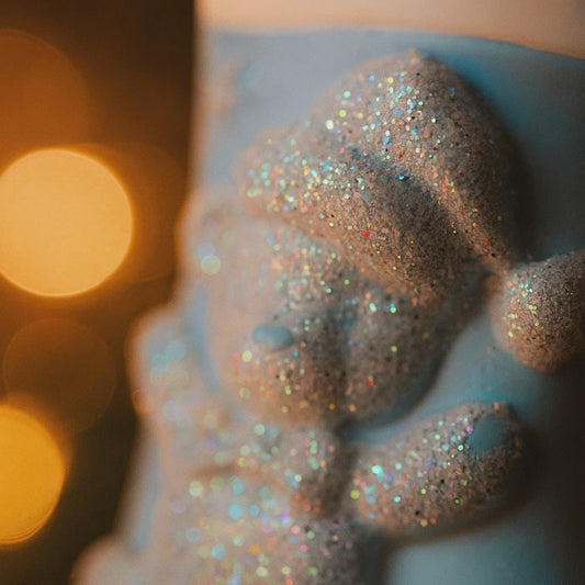 A glossy resin baby boy stocking ornament features a soft pastel blue Christmas stocking shape with a raised glitter style baby figure on the front, white cuff detail, small star accents, and smooth painted surfaces, surrounded by warm holiday lights and nursery themed props, handwritten personalization showing one baby name on the top cuff and the year written near the bottom of the stocking, designed as a mostly 2D ornament with raised 3D details on the front only.