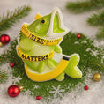 Load image into Gallery viewer, Decorative fish ornament with measuring tape around its neck on a festive background.
