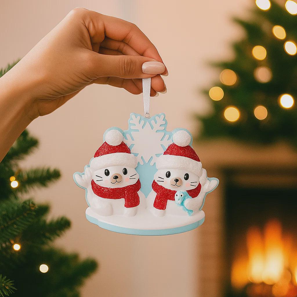 Hand holding a Christmas ornament with two cats in Santa hats against a festive background.