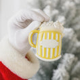 Load image into Gallery viewer, Yellow mug with white foam held by a gloved hand against a blurred natural background
