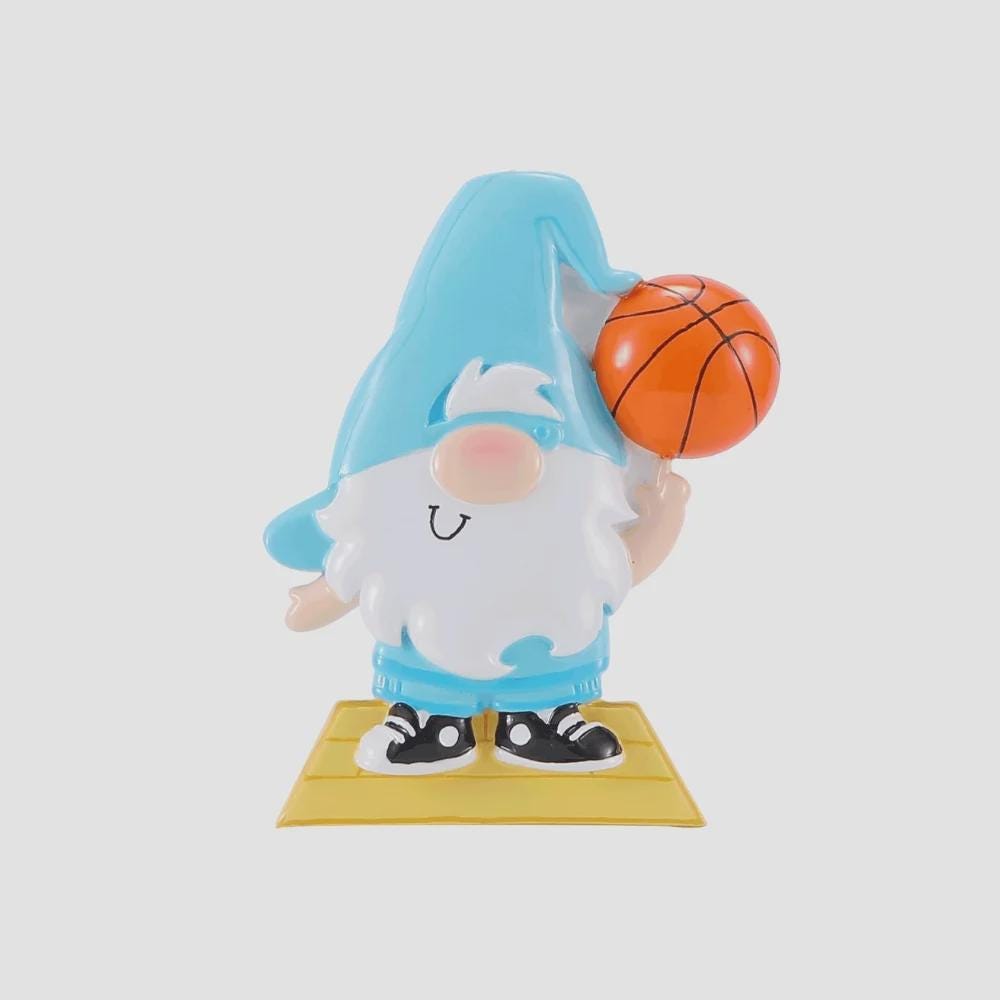 Personalized basketball gnome Christmas ornament featuring a cute blue gnome character holding a basketball, customizable name area on the hat and customizable year area on the base, glossy finish with raised 3D front details and flat 2D back, white hanging ribbon, displayed on a snowy holiday background with pine branches and festive decorations.
