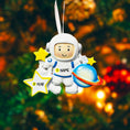 Load image into Gallery viewer, Personalized astronaut Christmas ornament featuring a detailed 3D front design with a smiling space explorer holding a colorful planet and bright yellow stars. The child’s name is added on the suit and the year is written on the star for a custom touch. This space themed ornament is perfect for kids who love rockets, planets, and outer space dreams. A fun and meaningful holiday keepsake for future astronauts and little space lovers.
