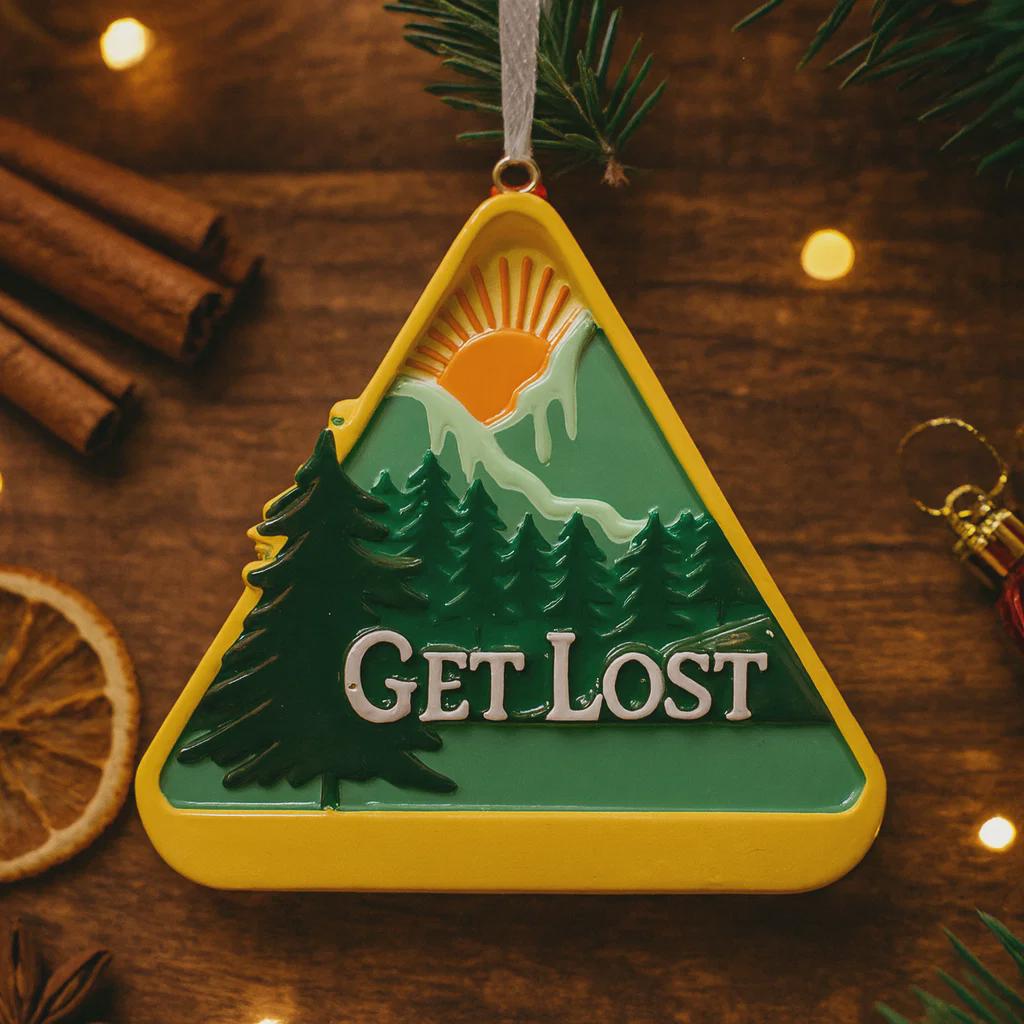 Decorative ornament with mountain and 'GET LOST' text on a wooden surface with cinnamon sticks and oranges.