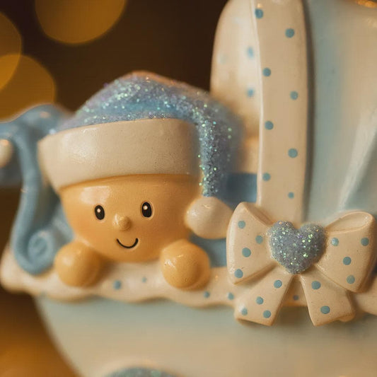 Personalized baby boy Christmas ornament featuring a light blue stroller with glitter details and a smiling baby wearing a blue nightcap. Custom name appears on the top and year on the bottom, making it a perfect Baby’s First Christmas keepsake. This blue resin holiday ornament is ideal for newborn boys, baby shower gifts, and celebrating a special first Christmas memory.