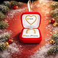 Load image into Gallery viewer, Personalized engagement ring ornament featuring a red velvet style ring box design with a sparkling diamond ring inside. The ornament includes free handwritten personalization with one name and year displayed inside the box. Designed with a smooth glossy finish and elegant gold details. Shown hanging with a ribbon in a festive holiday setting with snow greenery and warm lights. A romantic keepsake ornament perfect for Christmas trees engagements proposals and meaningful gift displays.

