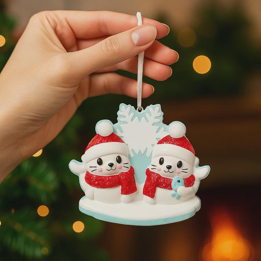 Hand holding a Christmas ornament with two snowmen wearing Santa hats and scarves against a blurred festive background.