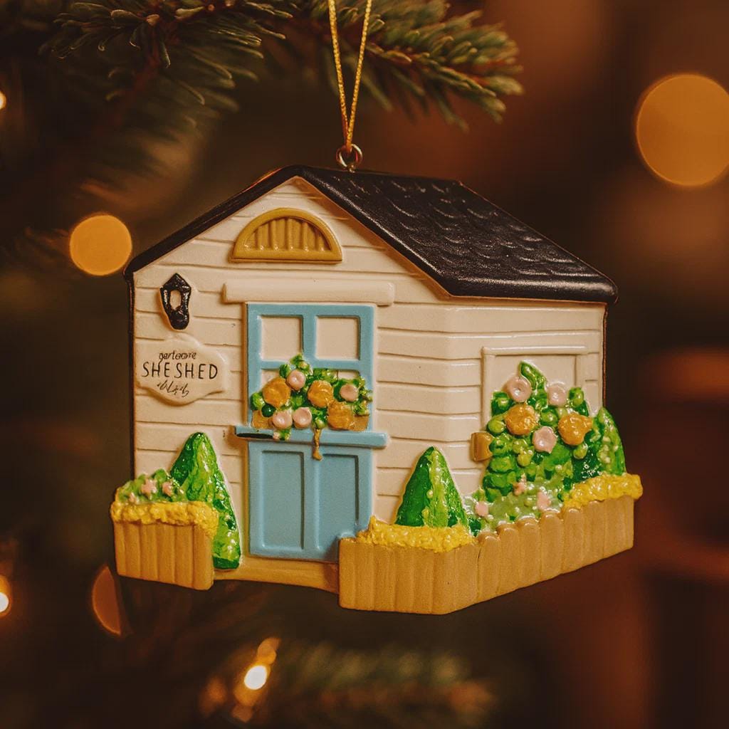 Decorative ornament of a small house with 'She Shed' sign on a tree.