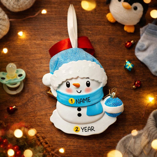 Personalized Snowman Baby Christmas Ornament featuring a cheerful snowman with blue glitter hat and scarf, holding a sparkling ornament. This design has a raised 3D front with textured details, dimensional elements, and vibrant winter colors. The child’s name is placed on the scarf and the year is added below. A perfect keepsake for baby’s first Christmas, newborn gift, winter holiday decoration, and meaningful family tree memory ornament.